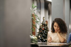 A young woman writing at a desk in a festive office with holiday decorations.